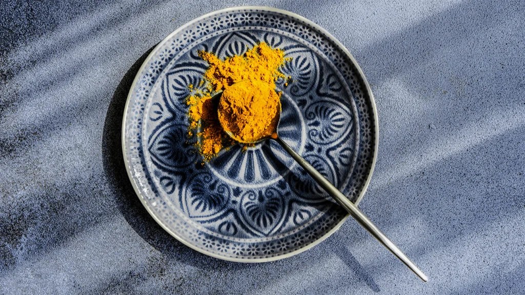 A teaspoon of turmeric powder on a plate.