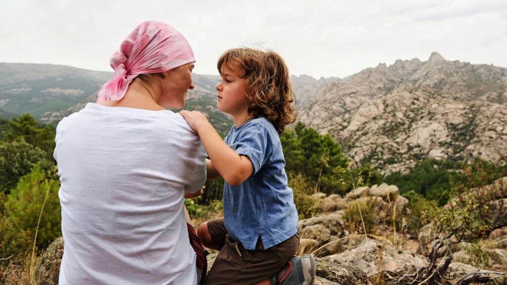 A woman with her head wrapped in a scarf looks at a child next to her while hiking on a mountain